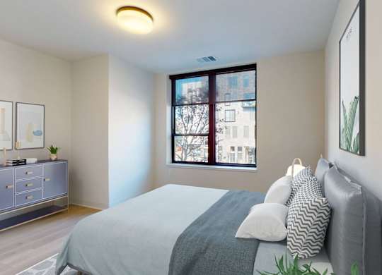A bedroom with a bed, nightstand, and a window with a view of a city.
