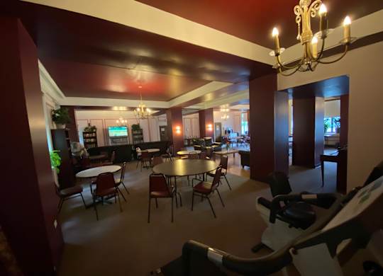 A room with a chandelier, tables, chairs, and a television.
