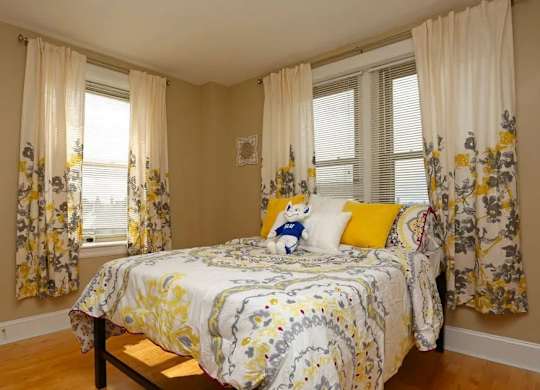 A bedroom with a bed in the center and floral curtains on the windows.