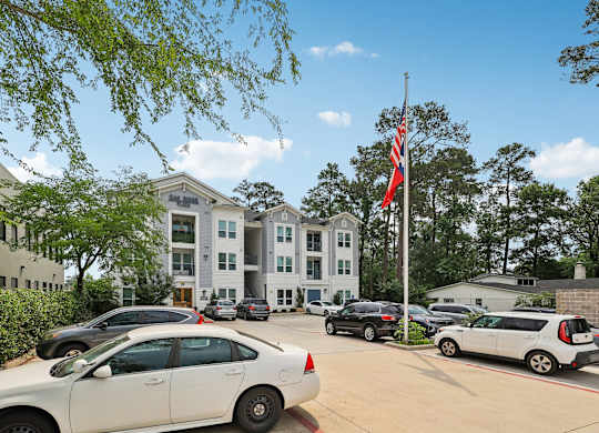A white car is parked in front of a building with a flag on a pole.