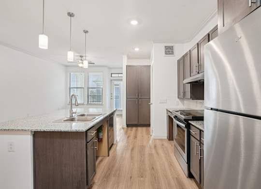 A modern kitchen with a refrigerator on the right and a sink with a window in the background.