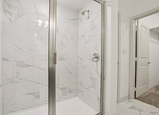 A white marble tiled bathroom with a glass door.