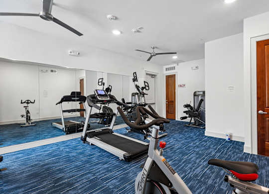 A gym with a variety of exercise equipment including treadmills, stationary bikes, and weight machines.