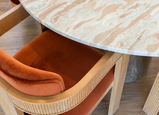A round marble table with orange chairs.