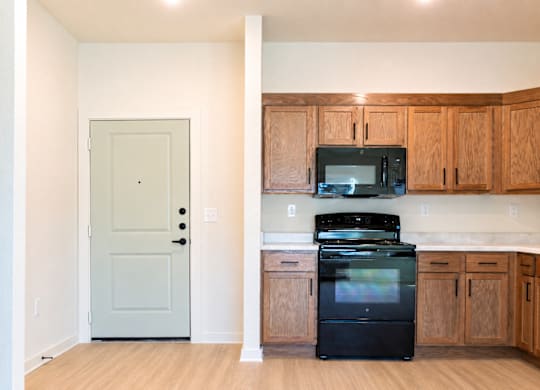 A kitchen with a black fridge and microwave, wooden cabinets, and a white door.
