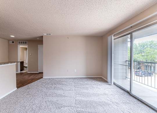 A spacious room with a carpeted floor and sliding glass doors leading to a balcony.
