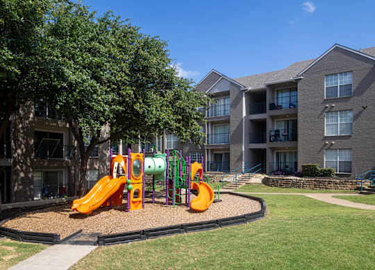 A playground with a slide and a climbing frame in front of apartment buildings.