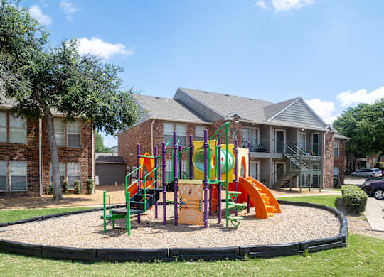 A playground with a slide, swings, and a seesaw in front of a building.