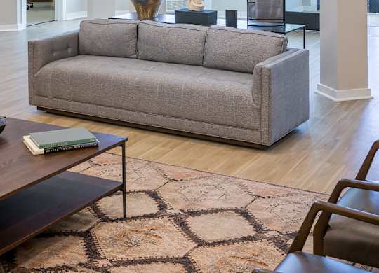 A grey couch sits in a well lit room with a coffee table in front of it.