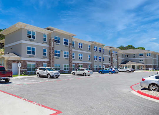A parking lot in front of a multi-story apartment building with cars parked.
