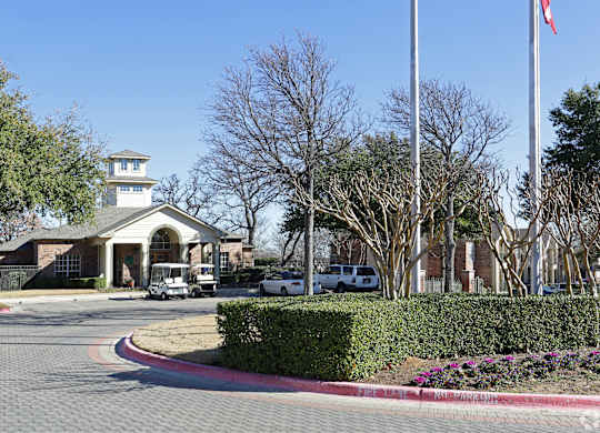 A building with a tower and a flag on top is surrounded by trees and has a driveway leading to it.