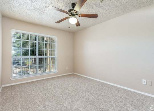A room with a ceiling fan and a window with blinds.