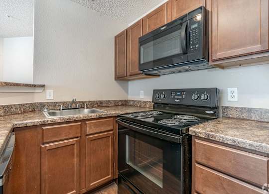 A black microwave oven is mounted above a black stove in a kitchen.