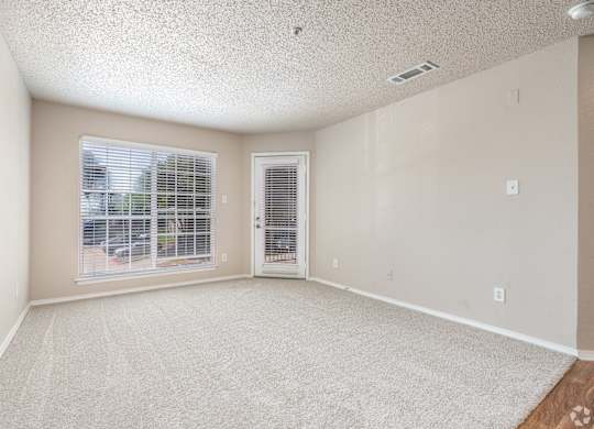 A room with a carpeted floor, a window with blinds, and a door with a window.