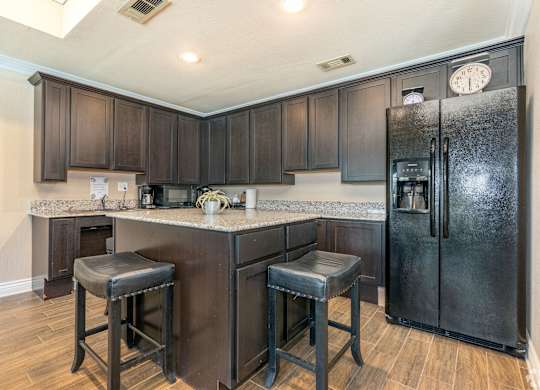 A kitchen with a black refrigerator and bar stools.