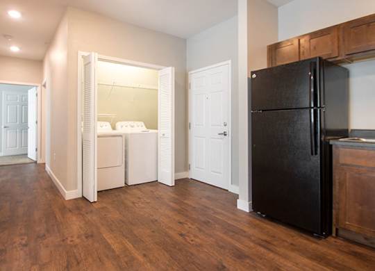 A black refrigerator sits in a kitchen with wood floors and white walls.