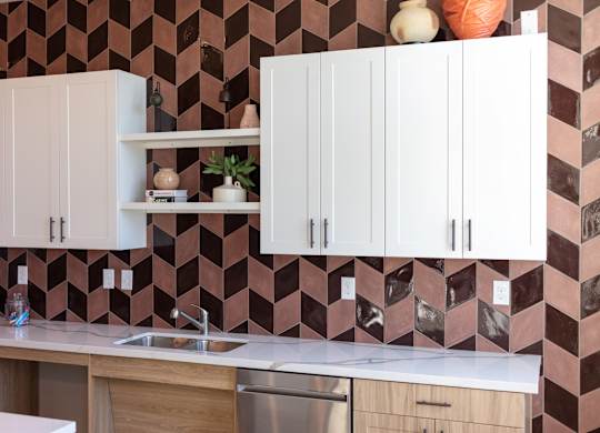 A kitchen with white cabinets and a brown tiled backsplash.