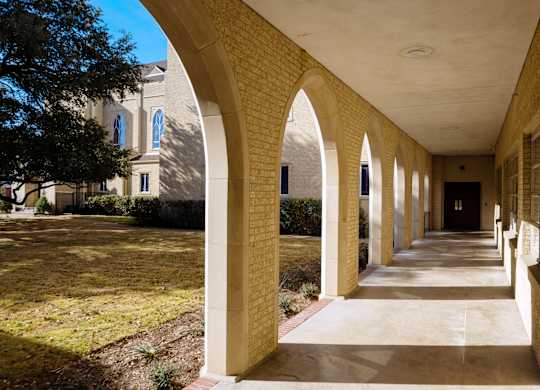 A long corridor with arched columns and a building in the background.