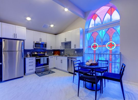 A kitchen with a table and chairs in front of a stained glass window.