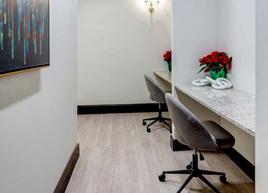 A hallway with a painting on the wall, a table with chairs and flowers on it, and a whiteboard.