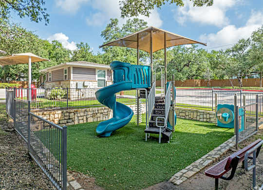 A playground with a blue slide and a yellow umbrella.