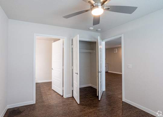 A room with a ceiling fan and three open doors.