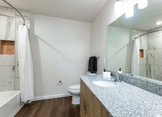 A white toilet sits in a bathroom with a marble counter top and a white shower curtain.