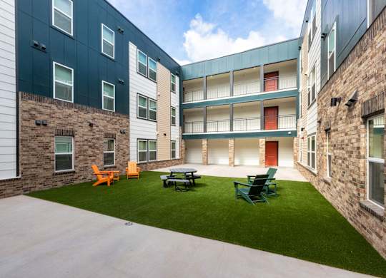 A courtyard with a lawn and chairs in front of a building.