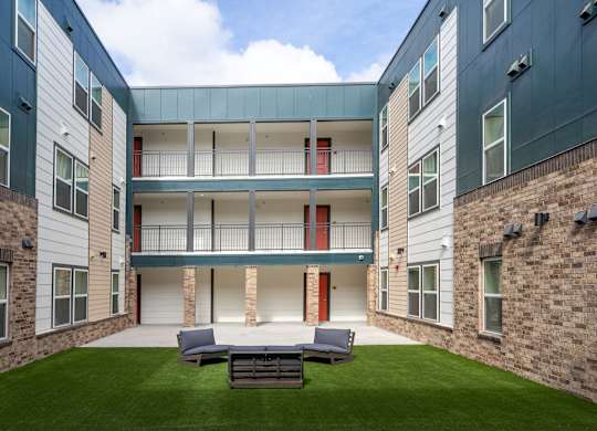A courtyard with a grass lawn and a bench in front of a building with a balcony.