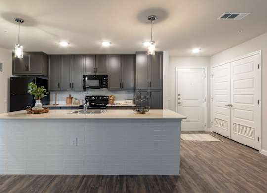 A modern kitchen with a large island and a black stove top oven.