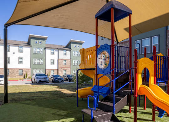 A playground with a slide and a play structure in front of apartment buildings.