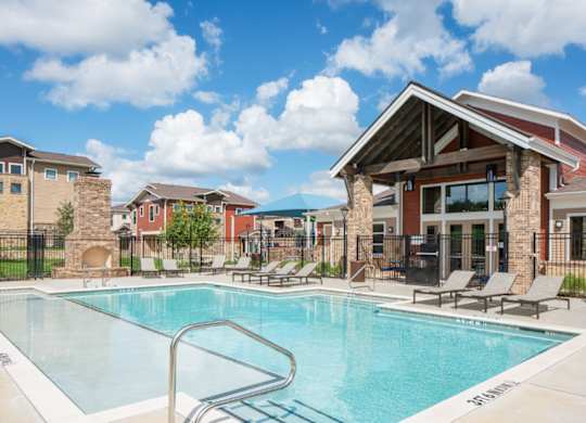A swimming pool surrounded by lounge chairs and buildings in the background.