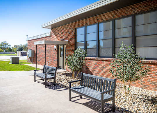 Three black benches are placed in front of a brick building.