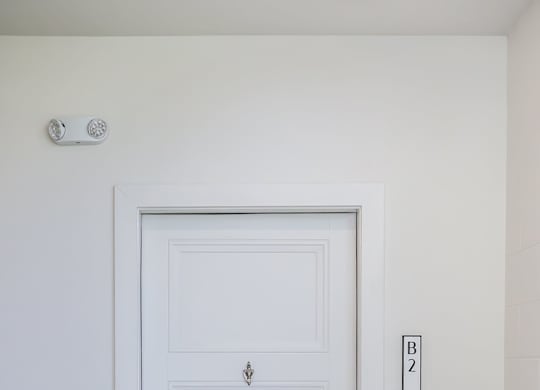 A white door with a silver handle and a small square plate on the wall above it.