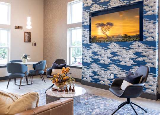 A living room with a large painting of a sunset on the wall.