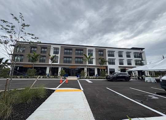 A parking lot in front of a multi-story building with a white canopy tent to the right.