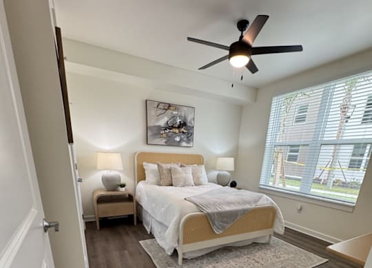 A bedroom with a bed, a ceiling fan, and a window with blinds.