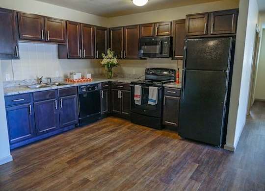 A kitchen with dark wood cabinets and a black fridge.