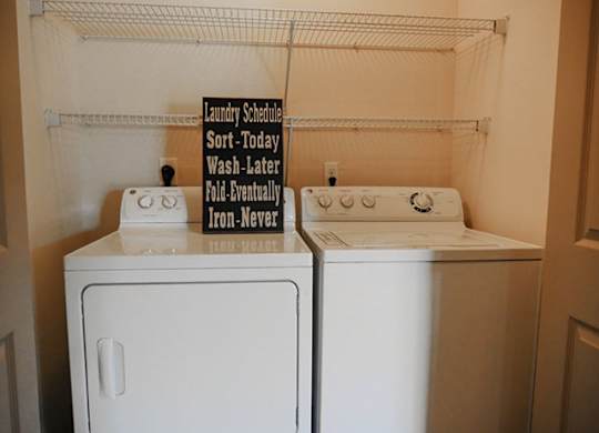 Two white front loading washing machines with a laundry schedule sign above them.