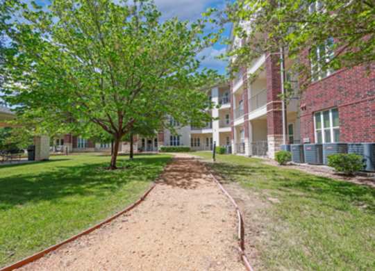 A tree in front of a building with a dirt path leading to it.