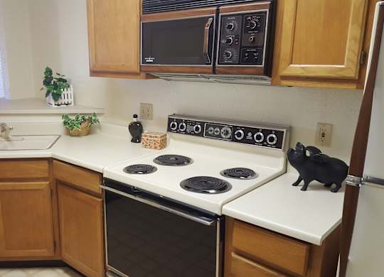 A kitchen with a black cat sitting on the stove.