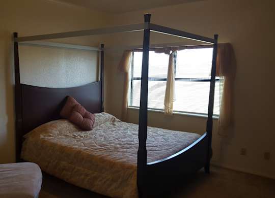 A bed with a white pillow and a white blanket is in the corner of a room.