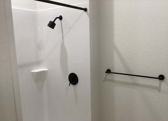 A white shower stall with a black shower head and a black bar.