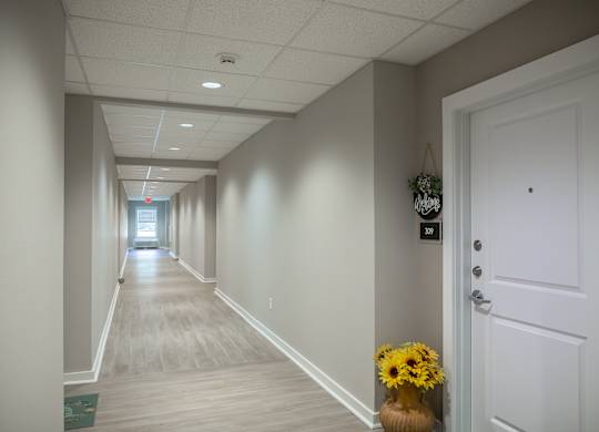 A long hallway with a door on the right and a vase of flowers on the floor.