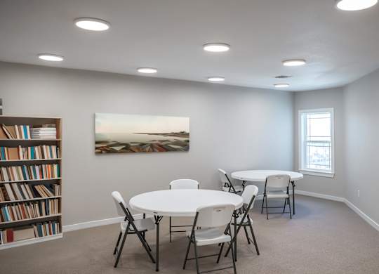 A room with a white table and chairs, a bookshelf, a clock, and a painting on the wall.