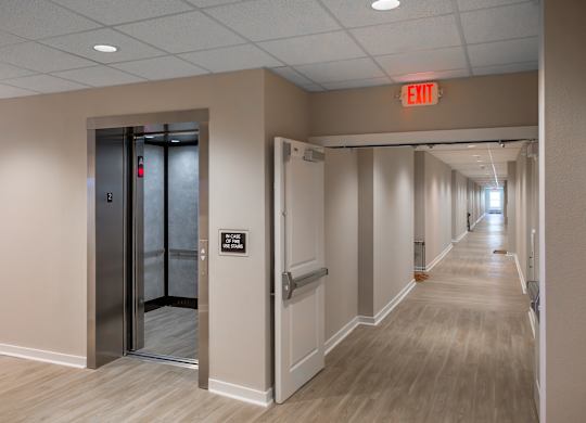 A hallway with a red exit sign above the door.