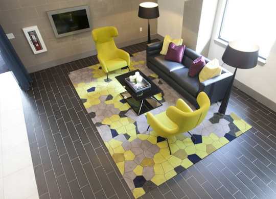 A yellow chair sits on a yellow and black tiled floor in a modern living room.