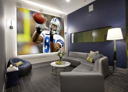 A football player in a blue and white uniform is catching a football in a modern living room.