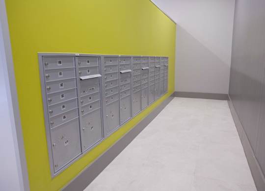 A row of mailboxes are lined up against a yellow wall.