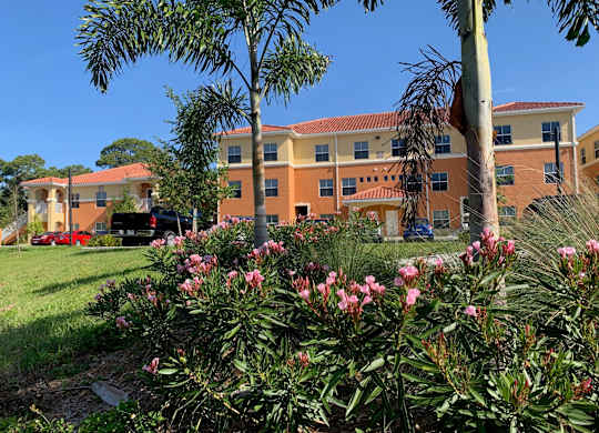 A building with orange walls and a red roof is surrounded by greenery and trees.